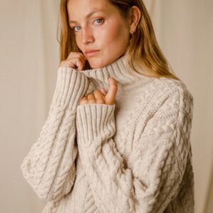 Photo cadré serré du haut du pull CHIARA Beige. La mannequin est lovée dans son pull et resserre le col montant contre elle